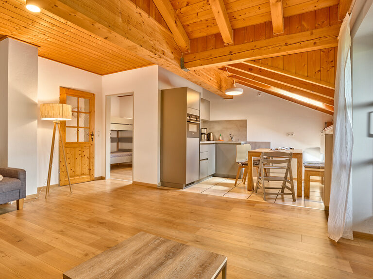 Wohnzimmer und Küche einer Ferienwohnung im Landhaus Lerchenweg mit rustikalem Holzboden, Dachbalken und gemütlicher Einrichtung