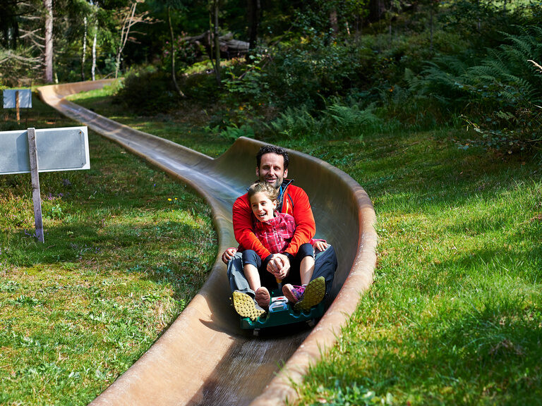 Sommerrodelbahn am Silberberg Ein Mann fährt mit einem Kind die Silberberg Rodelbahn hinunter.